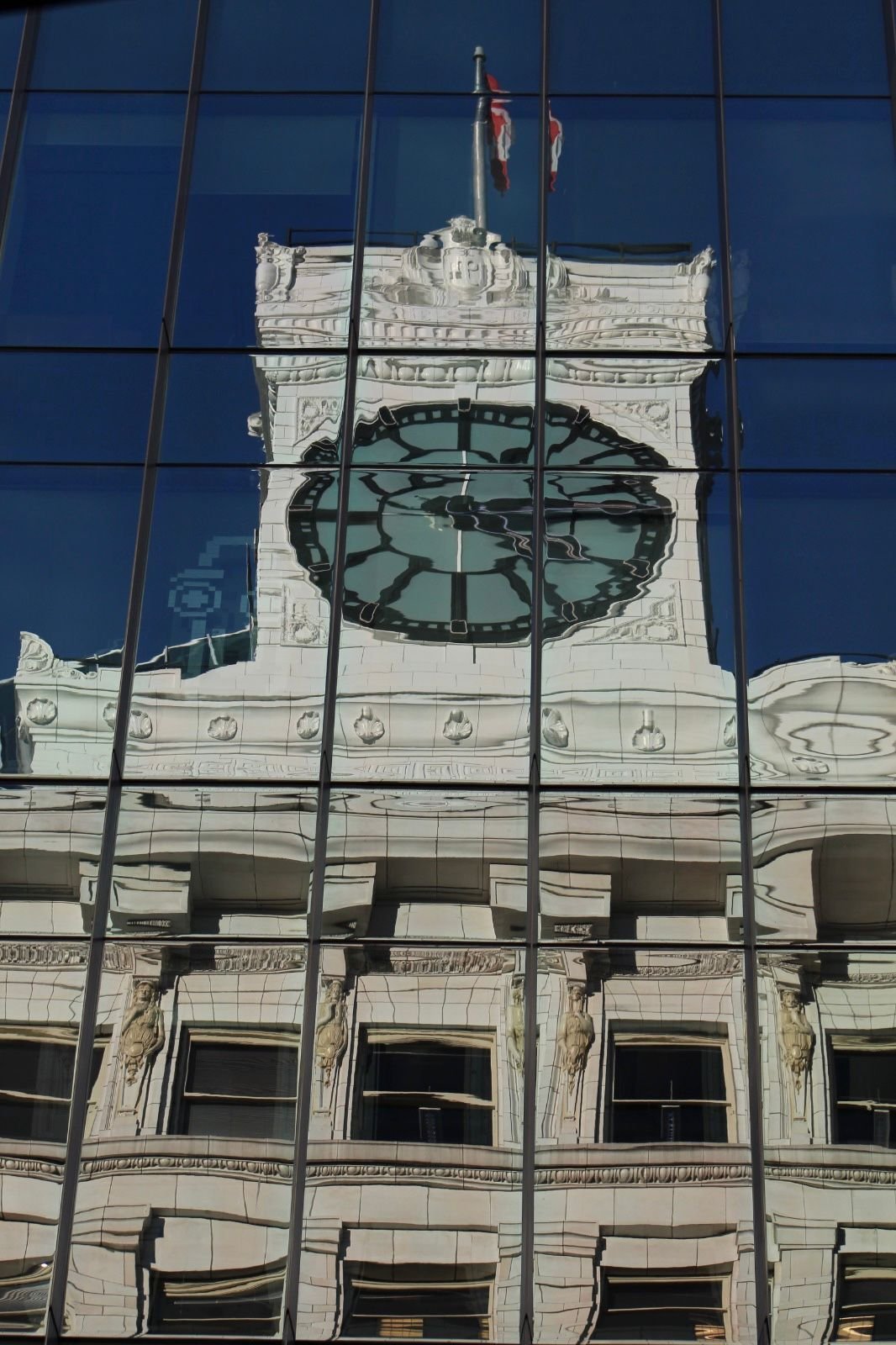 Historic clock tower reflected and distorted in a modern glass facade