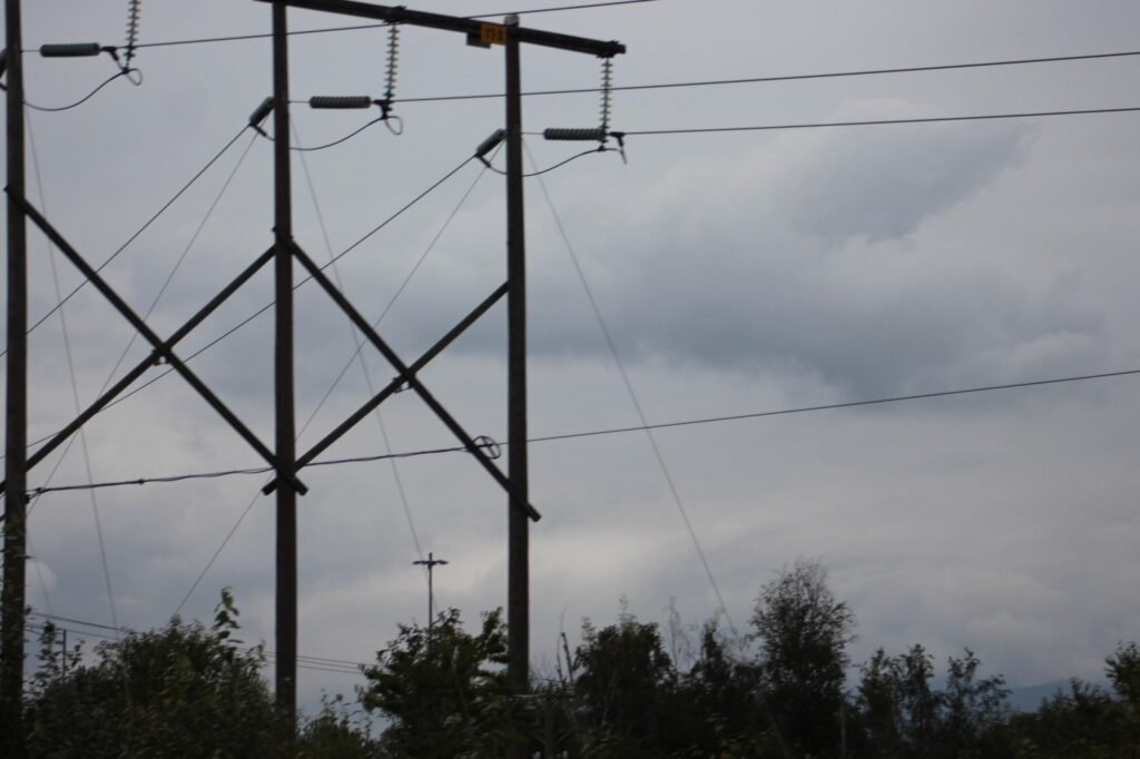Overhead power lines and utility structures crossing against a cloudy sky
