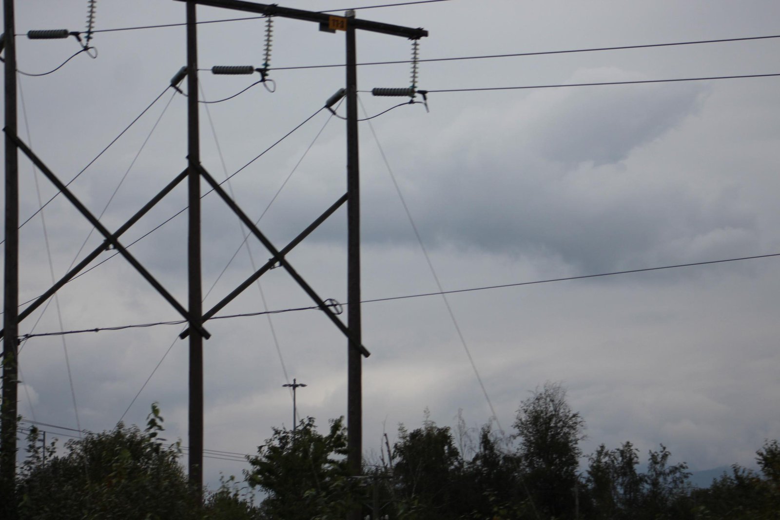 Overhead power lines and utility structures crossing against a cloudy sky
