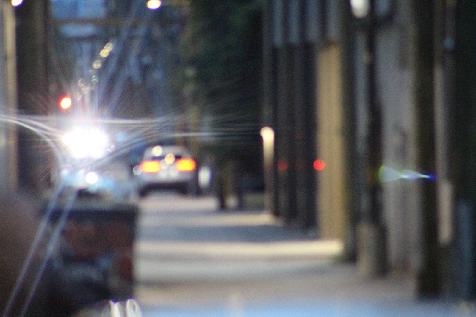 Bright car headlights flare along a softly blurred city street — Joe Passage