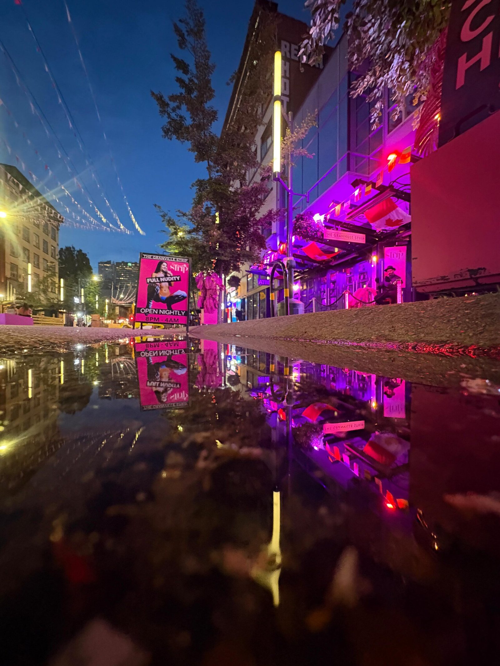 Neon-lit Vancouver street reflected in a rain puddle at night
