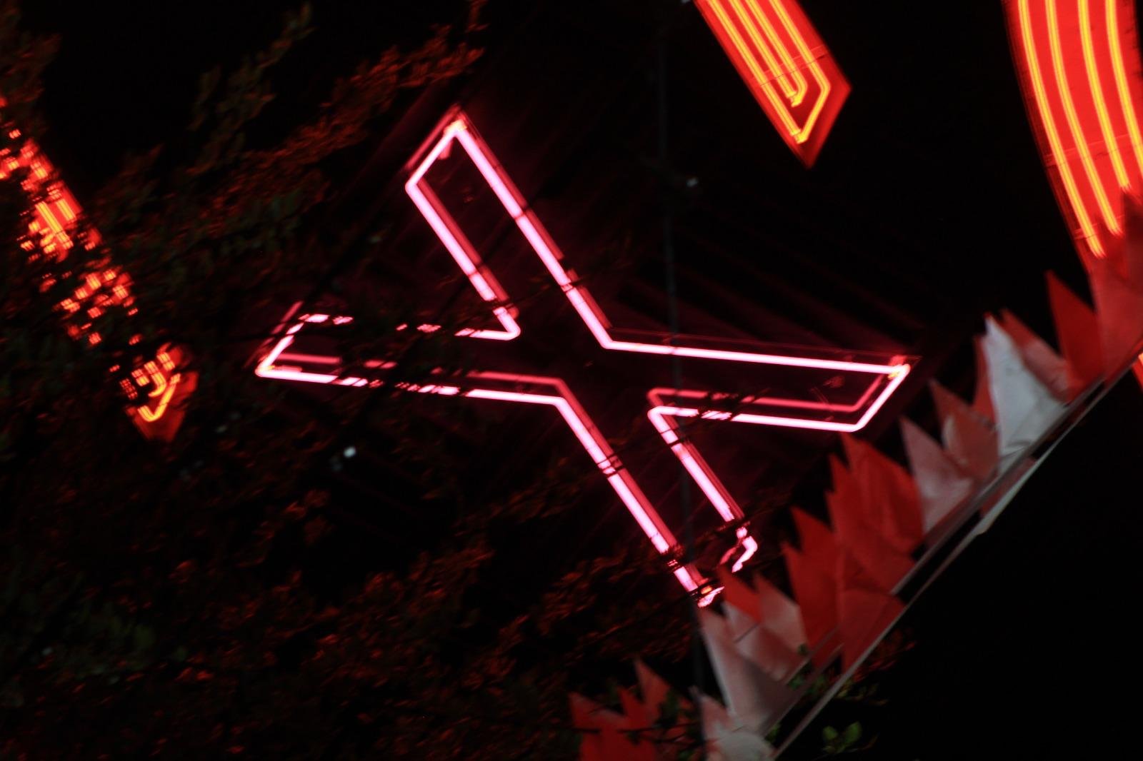 Red neon X sign glowing against the dark night — Joe Passage