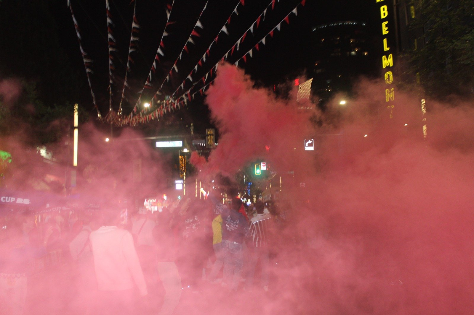People moving through a cloud of pink smoke on a city street at night — Joe Passage