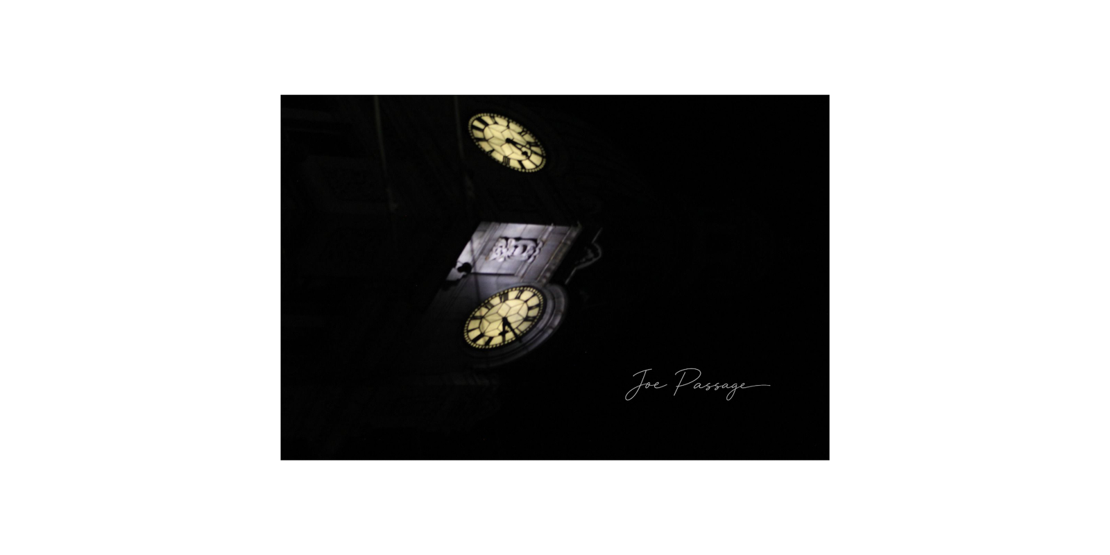 Two illuminated clock faces emerging from darkness in an urban night scene.