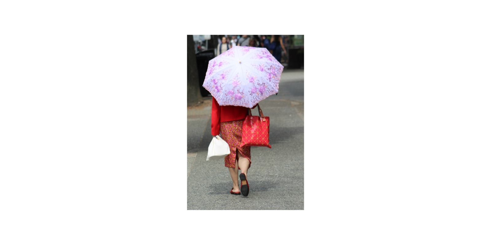 A woman walking away beneath a pink floral umbrella on a city street.