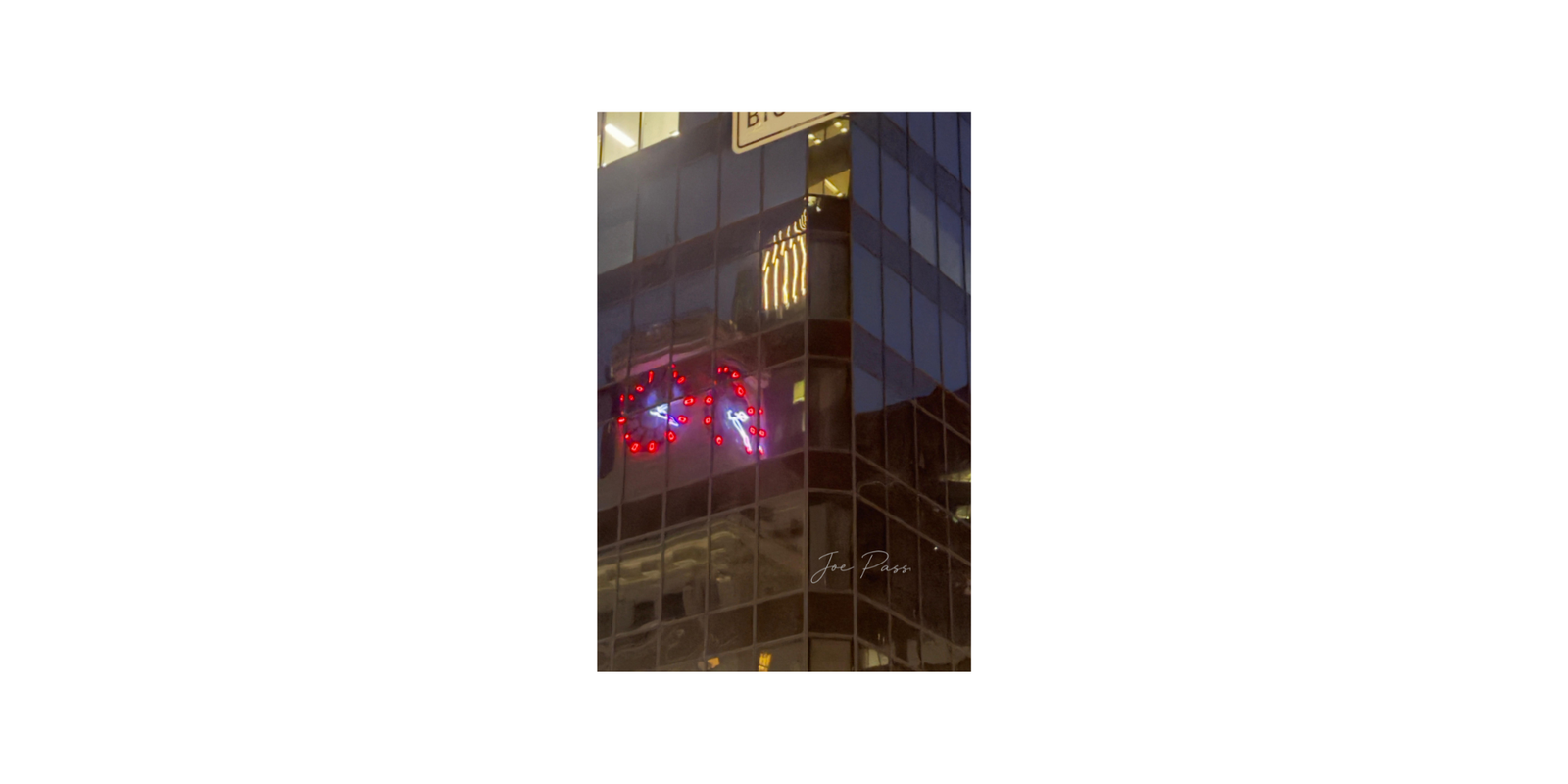 Red illuminated clock reflected in the glass facade of a city building at night.